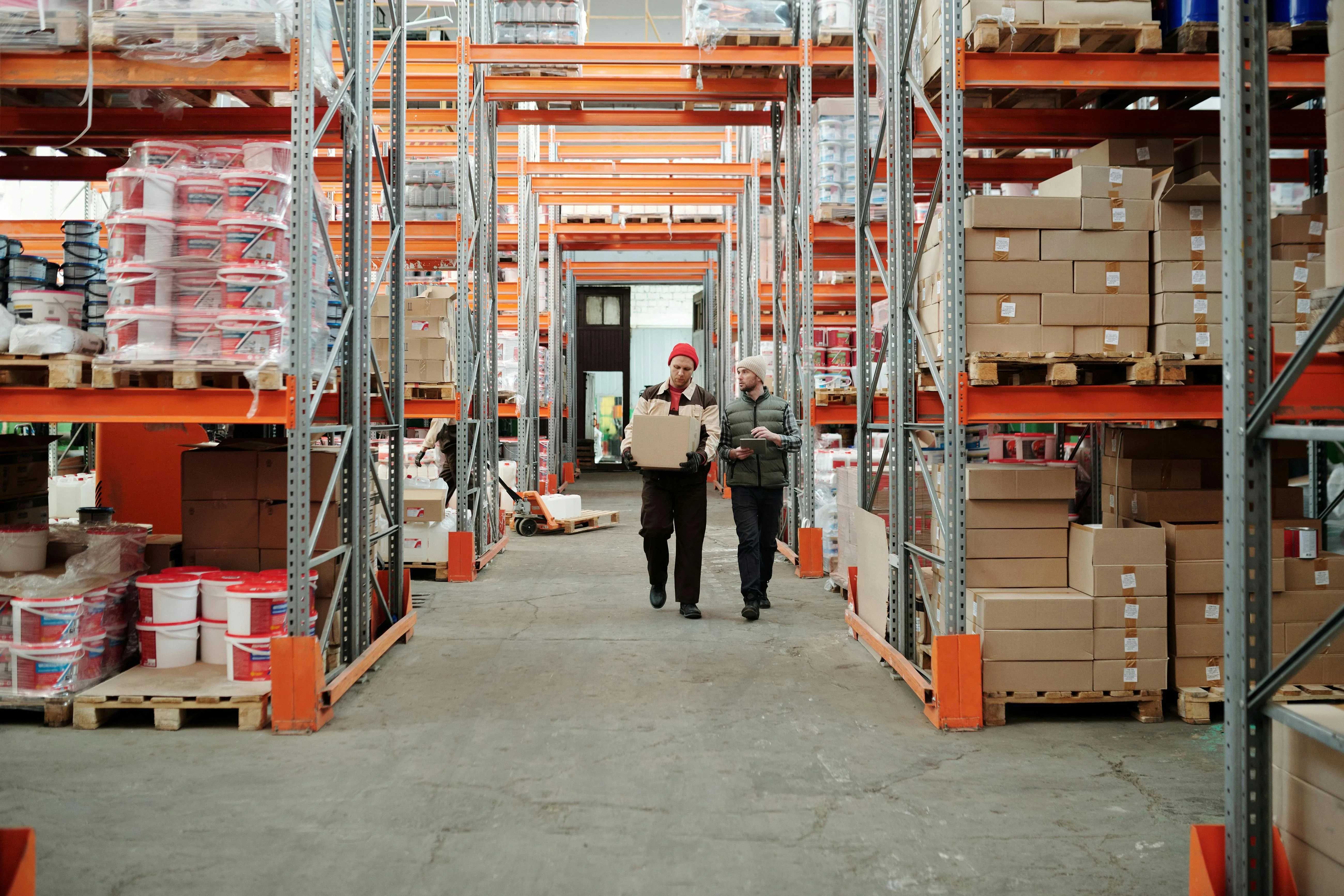 Two warehouse workers walking through stocked inventory shelves handling a package for order fulfillment
