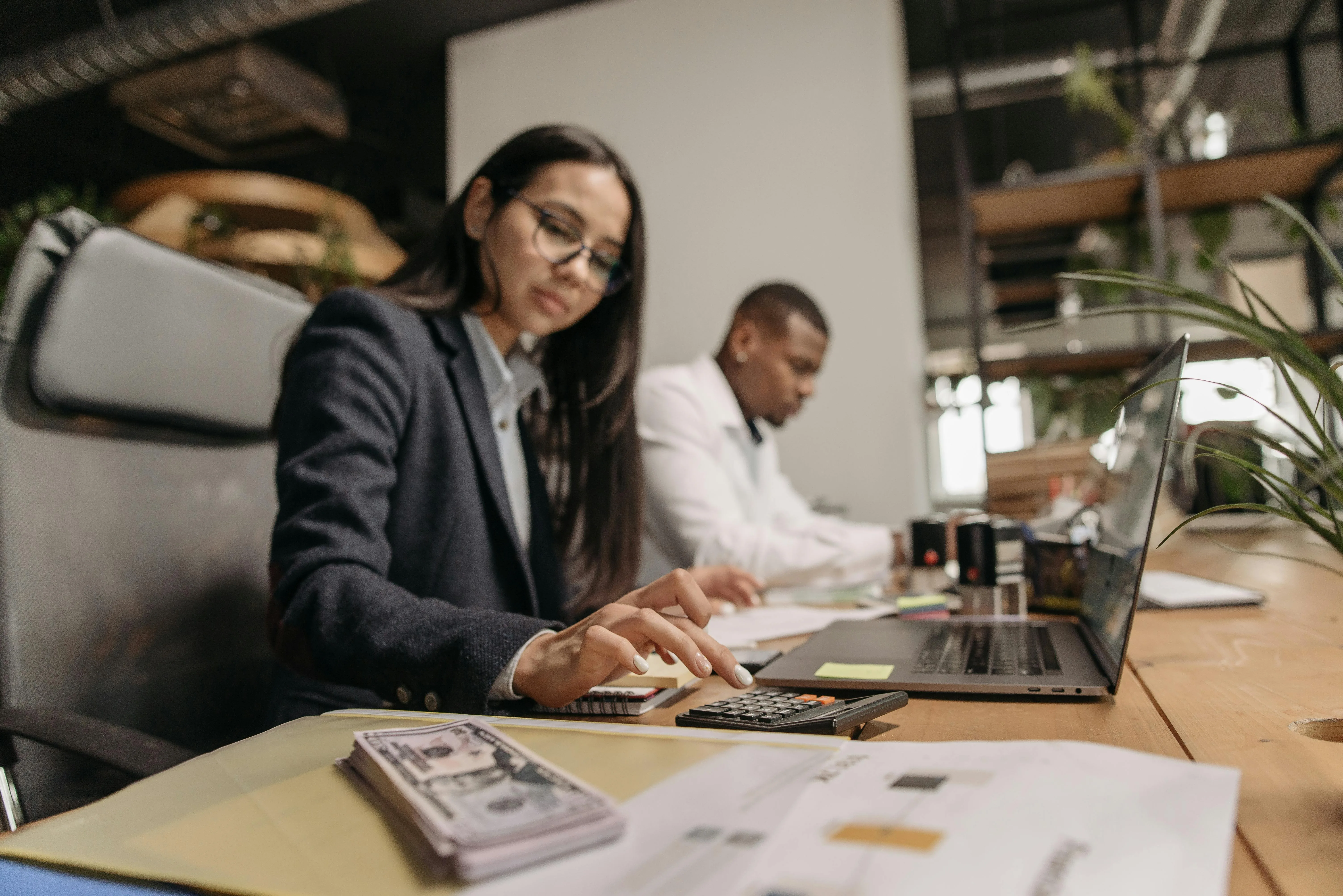 Two financial professionals collaborating at a desk with a laptop and calculator in a modern office