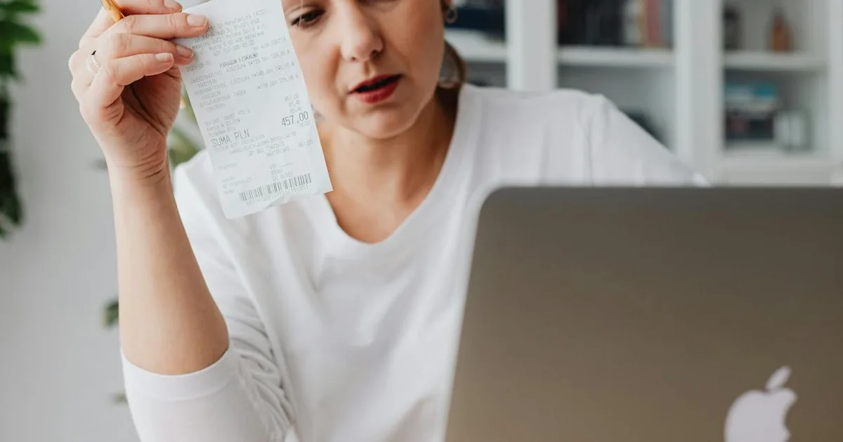 Business owner reviewing financial expenses on laptop with receipts at desk — Shopify fees tracked in QuickBooks Online expense accounts