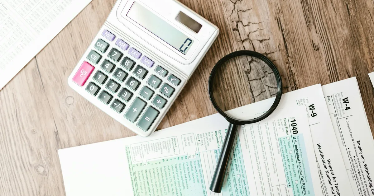 Calculator and magnifying glass beside tax documents on a desk — Shopify sales tax and QuickBooks Online tax reporting for US merchants